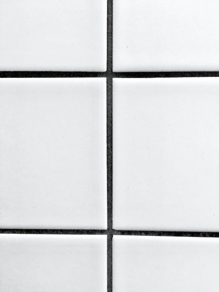 Close-up view of a white square tile wall with black grout lines forming a grid pattern.
