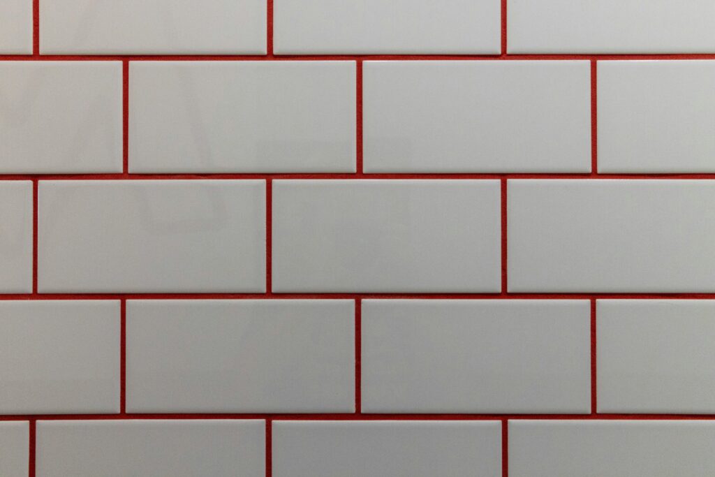 Close-up view of a white subway tile wall with bright red grout lines arranged in a staggered brick pattern.