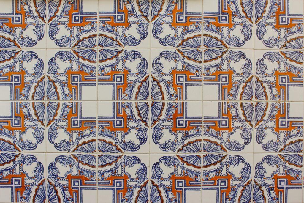 Close‑up of ornate ceramic tiles featuring blue floral motifs and orange geometric accents in a repeating symmetrical pattern.